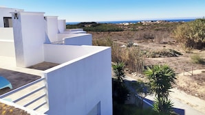 A white building with a clear view of the sea and hills in the background. - Sea View Terrace Wellness Apartment - Duna Parque Group (Odemira)