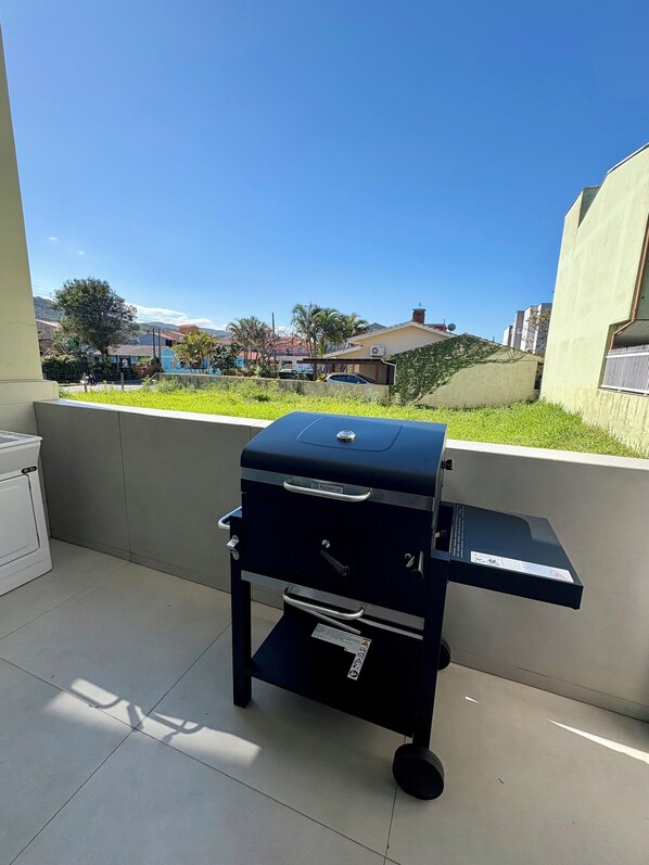 A barbecue grill on a balcony with a view of houses and greenery.