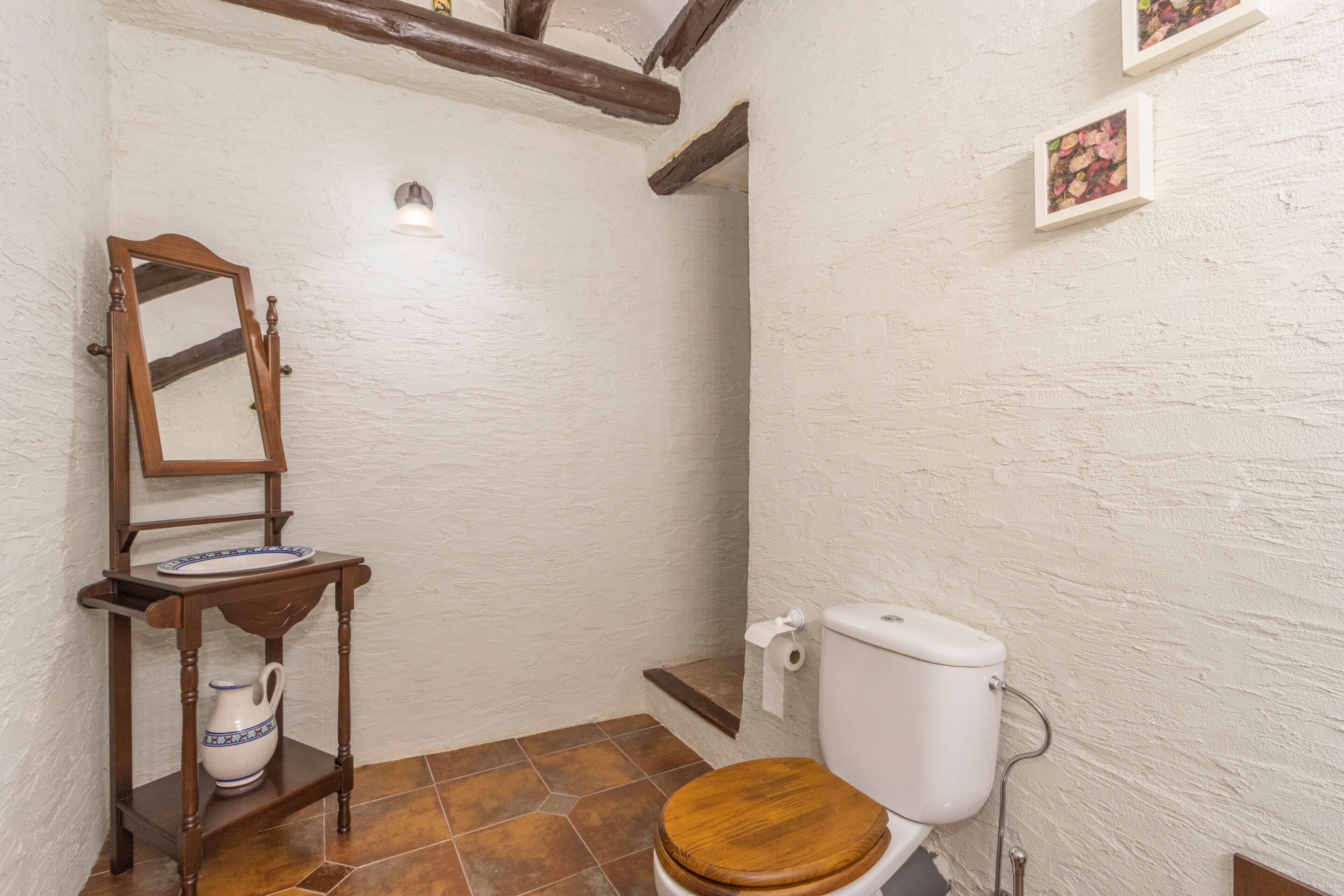 Un bagno con un water in legno, un mobile lavabo in legno con un lavabo, uno specchio e un lampadario a parete.