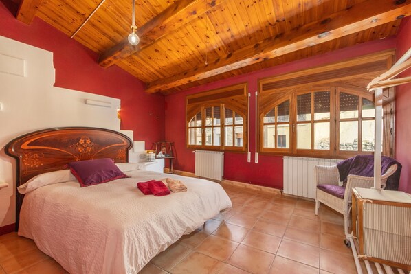 Un dormitorio con techo de madera, una cama con cabecera, una ventana con vistas y una silla.
