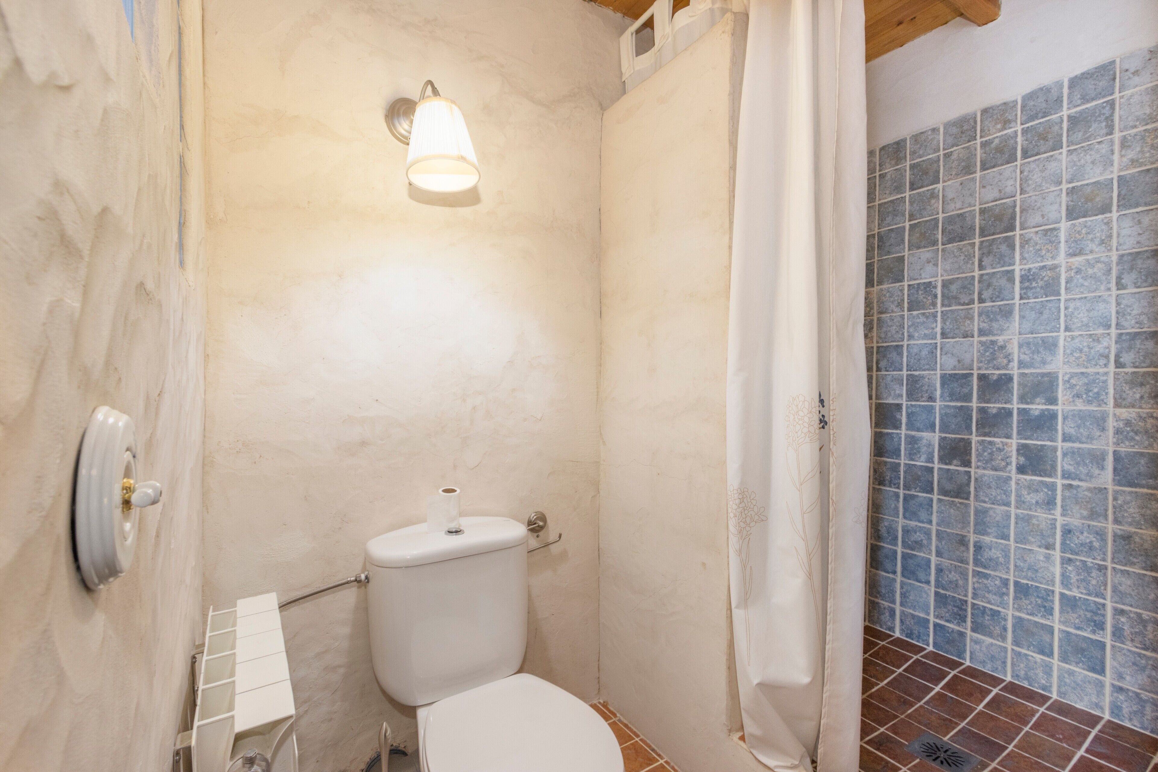 A bathroom with a toilet, a shower curtain, a tiled wall, and a light fixture.