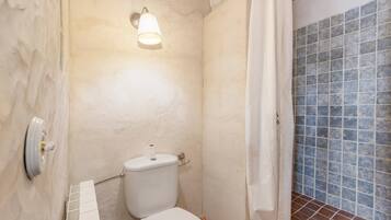 A bathroom with a toilet, a shower curtain, a tiled wall, and a light fixture.