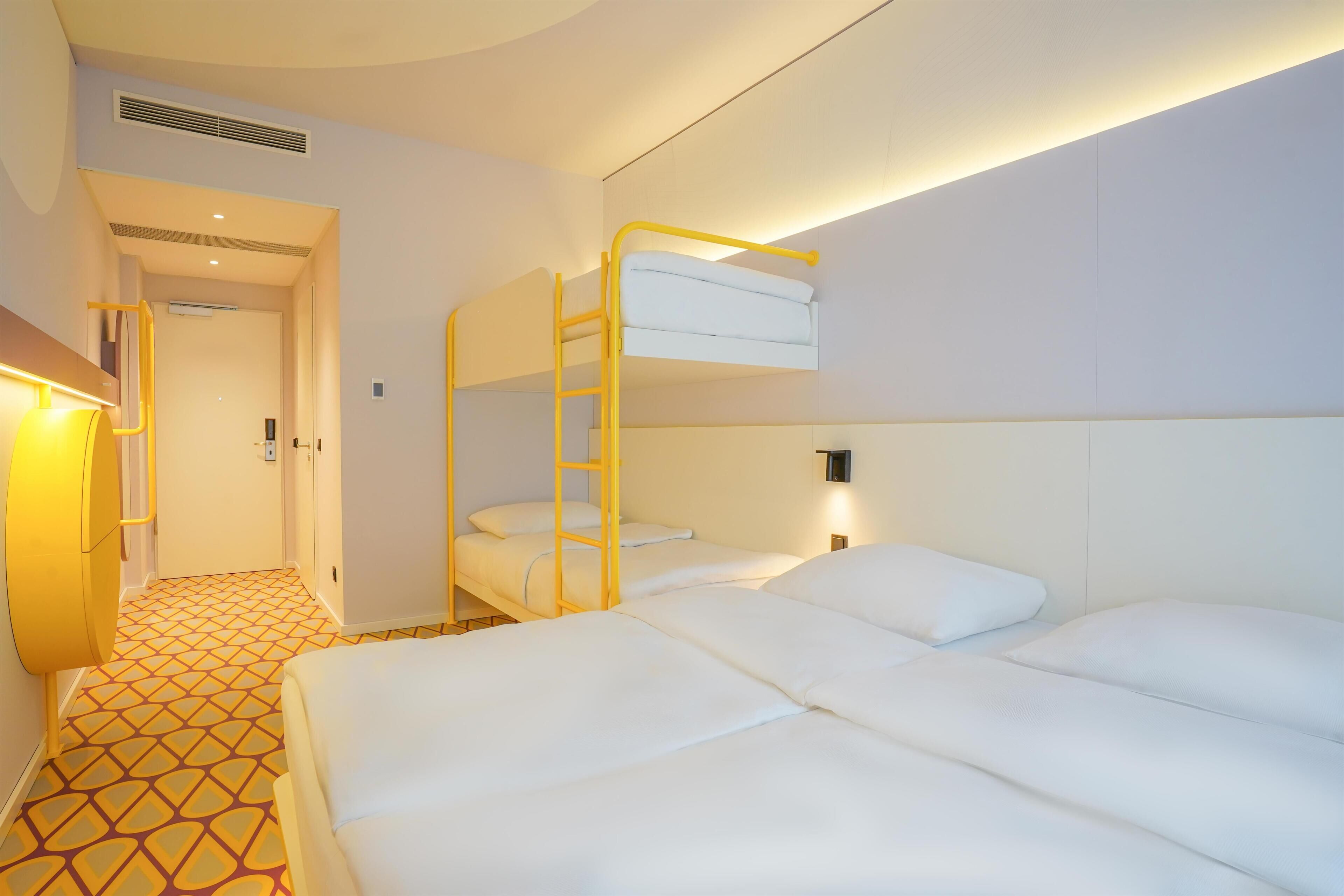Una habitación de hotel con literas, una cama individual, un piso estampado y un pasillo que lleva a una puerta.