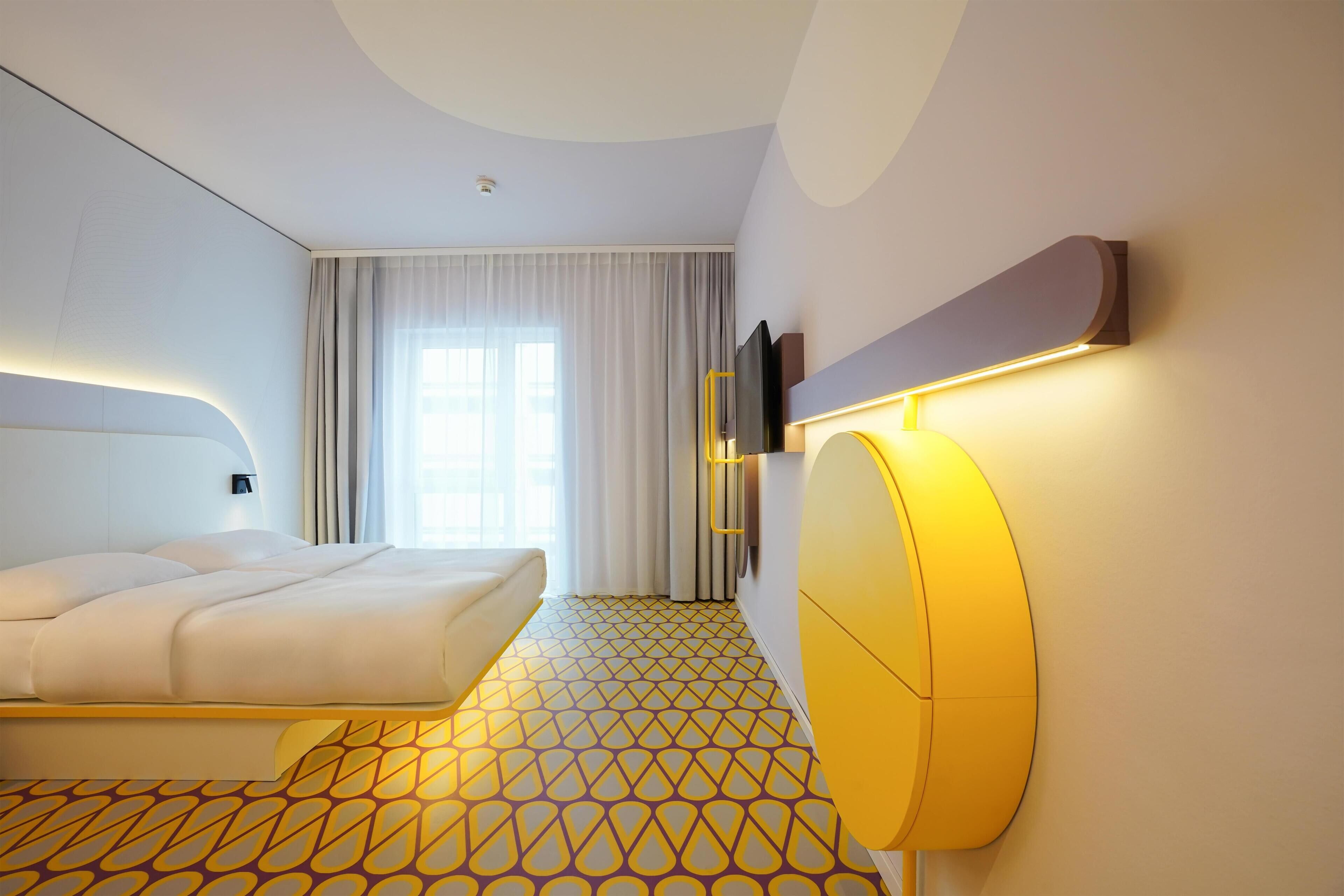 Ein modernes Hotelzimmer mit einem großen Bett, einem flachbildfernseher an der Wand und einem gemusterten Boden.