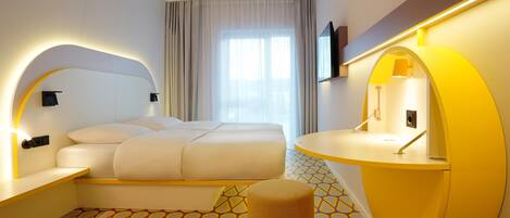 Una habitación de hotel moderna con una cama grande, una mesita de noche, un pequeño taburete, un escritorio curvo y un ventanal con cortinas.