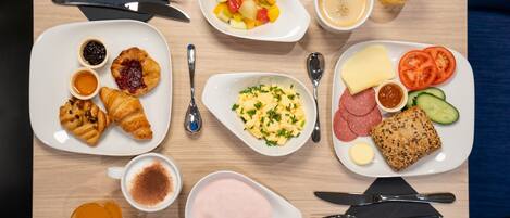 A breakfast table with croissants, fruit, scrambled eggs, toast, and various spreads.