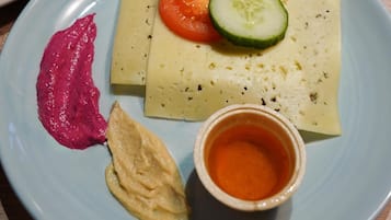 Un plato con un sándwich, una rodaja de tomate, un pepino, una cucharada de salsa roja, una cucharada de salsa amarilla y una taza pequeña de salsa naranja.