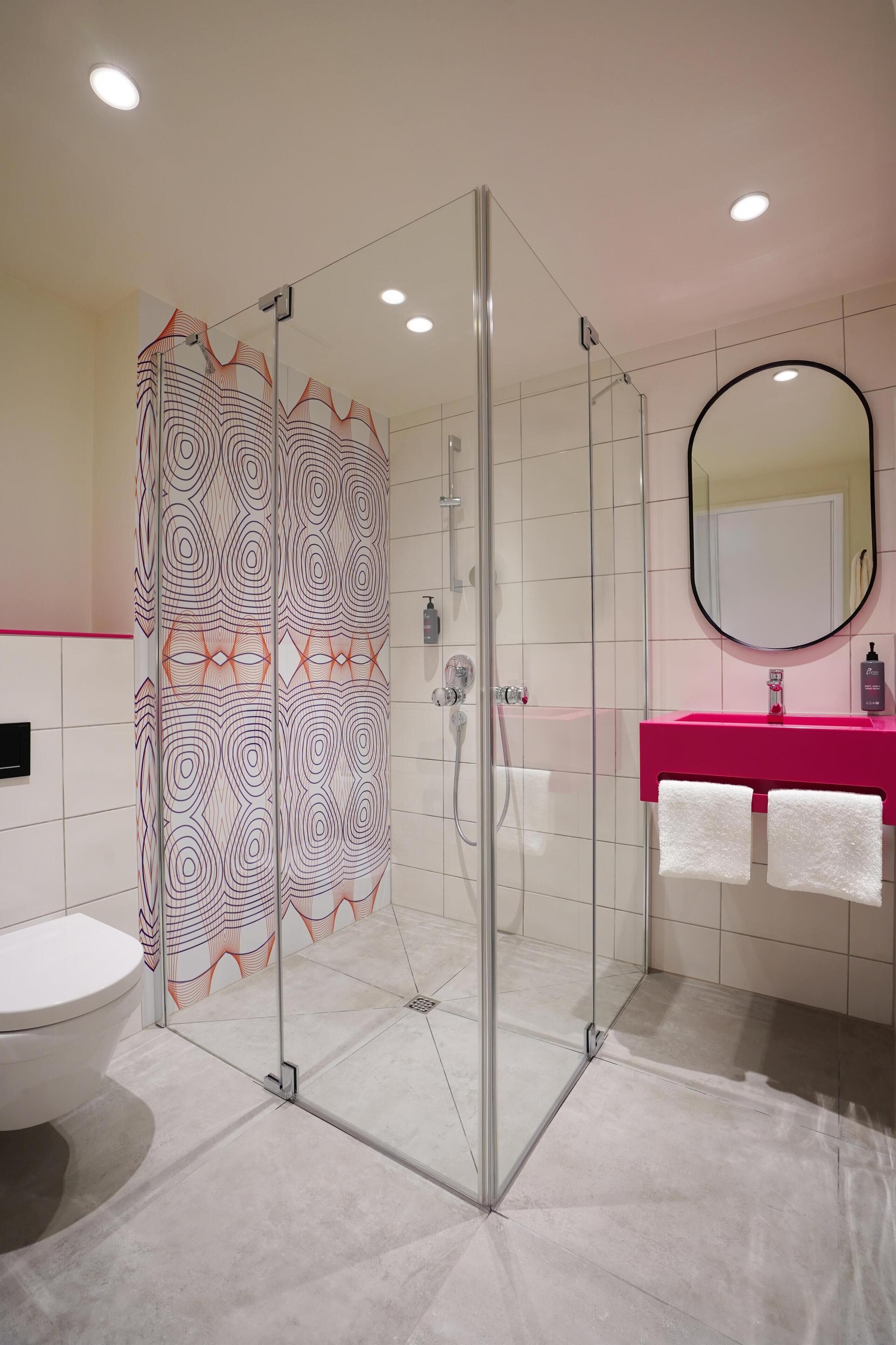 Een moderne badkamer met een glazen douchecabine, een wit toilet, een roze wastafel en een spiegel.