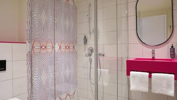 Une salle de bain moderne avec une douche à parois de verre, des toilettes blanches, un lavabo rose et un miroir.
