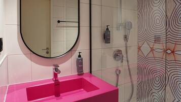 Ein Badezimmer mit einem rosa Waschbecken, einem großen Spiegel, einer Dusche und Wandfliesen mit Muster.
