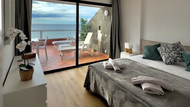 Ein Schlafzimmer mit einer großen Schiebeglastür, die auf einen Balkon mit Meerblick führt.