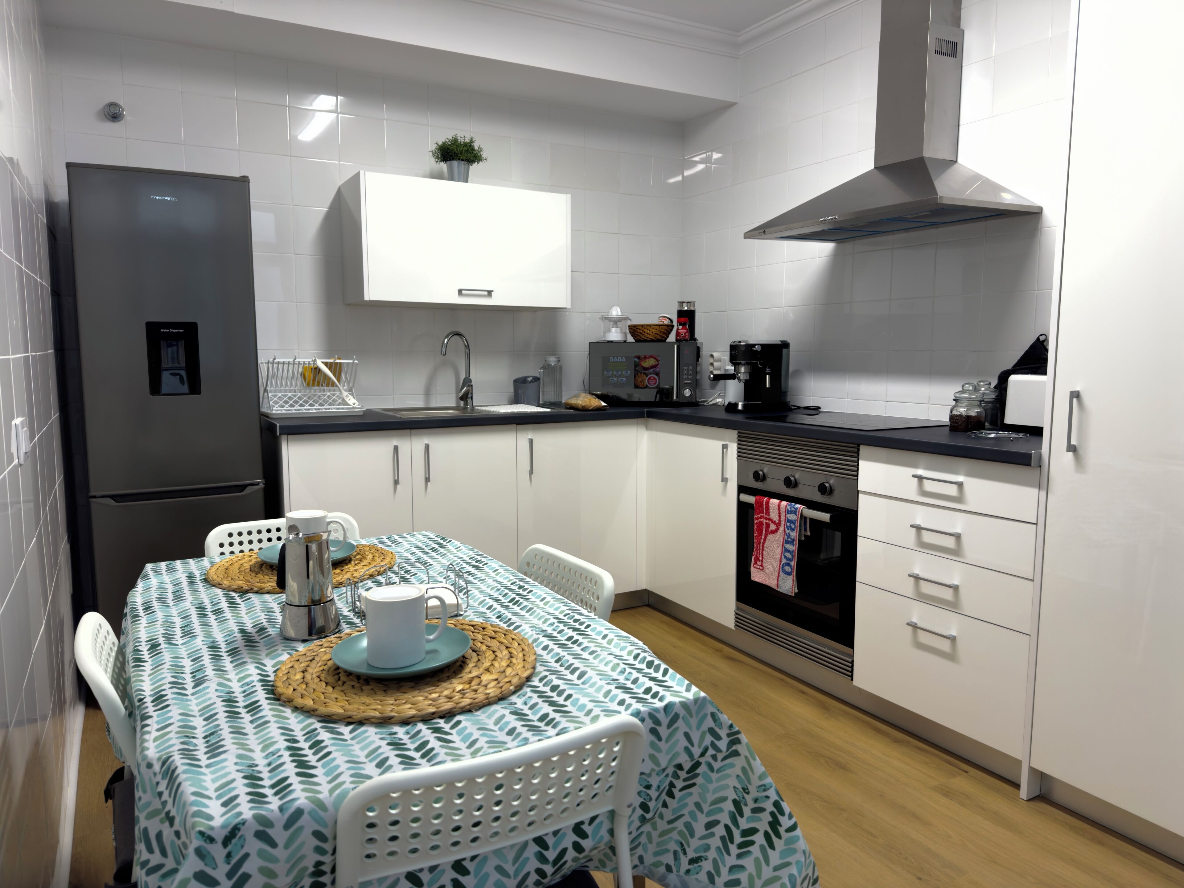 A modern kitchen with white cabinets, a stainless steel refrigerator, a coffee machine, and a small oven.