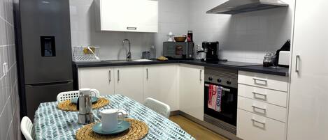 A modern kitchen with white cabinets, a stainless steel refrigerator, a coffee machine, and a small oven.