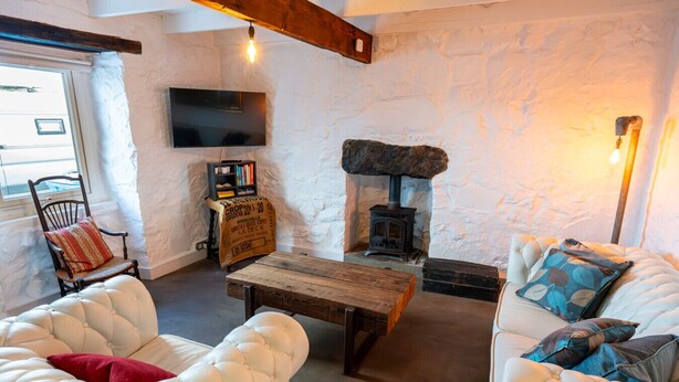 Ein gemütliches Wohnzimmer mit Kamin aus Stein, einem an der Wand befestigten Fernseher und einer komfortablen Sitzecke mit Sofa und Sesseln.