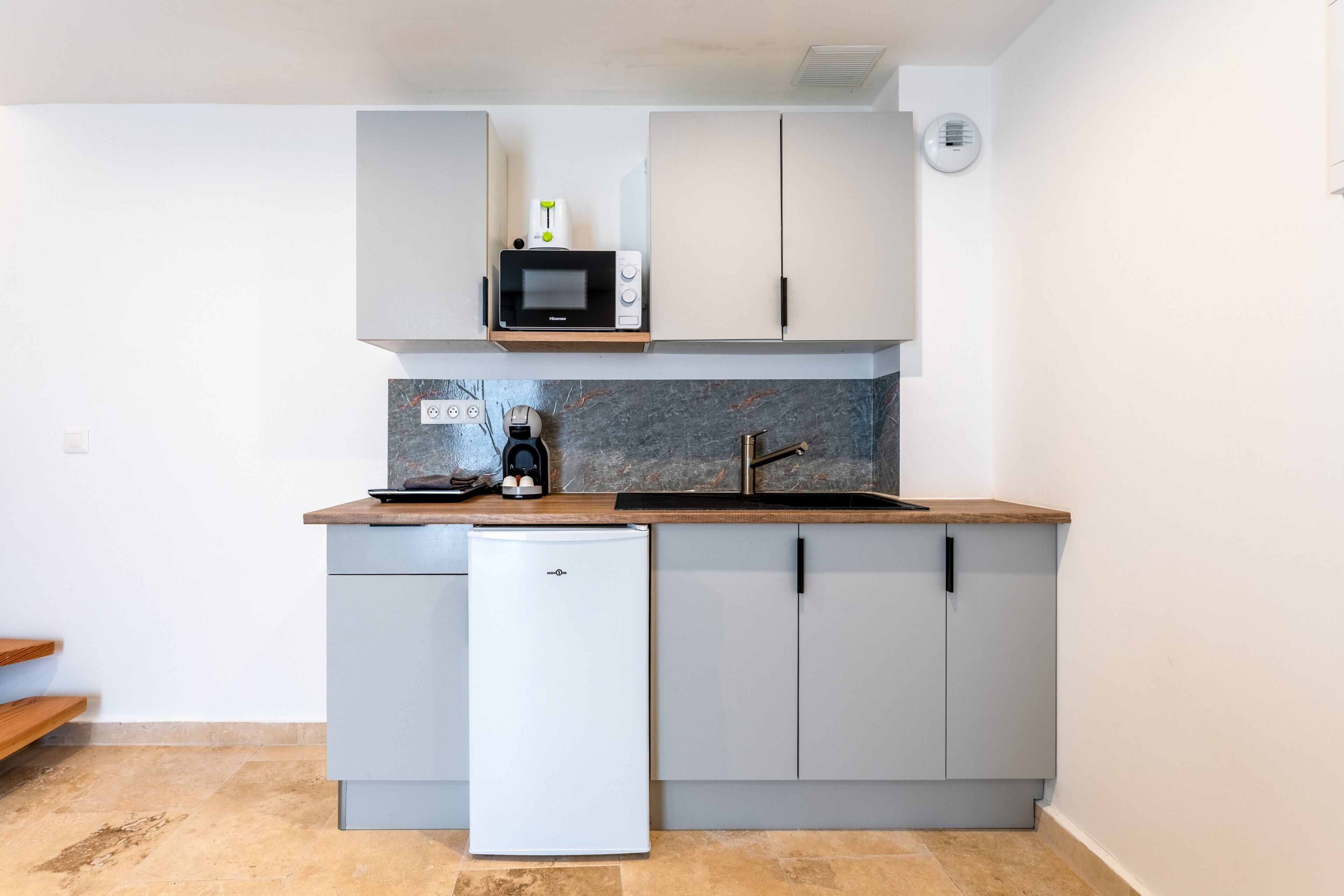 Una cocina compacta con microondas, cafetera y un refrigerador pequeño.