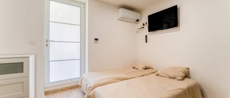 A bedroom with two beds, a TV, an air conditioning unit, and a sliding door.