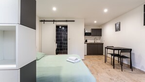 Una habitación compacta con cama, una kitchenette pequeña, una mesa de comedor con sillas y un baño con ducha.