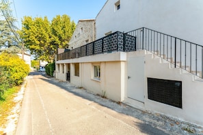 A building with a white exterior, a black metal railing on the upper floor, and a paved street in front. - Studio Apartment 'Canto Cigalo Rdc 3' with Wi-Fi and Air Conditioning (Robion)