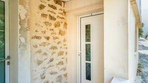 Una habitación con pared de piedra, una puerta blanca con paneles de vidrio y un escalón pequeño que lleva a la puerta.