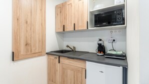 Eine kompakte Küche mit Holzausstattung, einer schwarzen Mikrowelle, einer Kaffeemaschine und einem kleinen Kühlschrank.