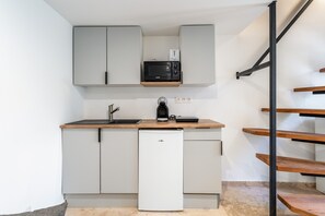 A compact kitchen with a microwave, toaster, and coffee maker on a wooden countertop, above white cabinets, and a dishwasher below.