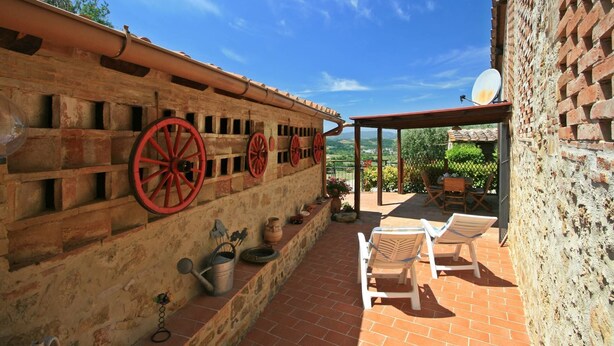 A patio area with a brick wall, red wheel spindles, outdoor furniture, and a satellite dish. - Casalecchi - Cottage between Siena & Florence (Staggia)