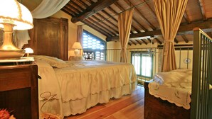 A bedroom with a wooden ceiling, a large bed with a white bedspread, a nightstand with a lamp, and a window with curtains. - Casalecchi - Cottage between Siena & Florence (Staggia)