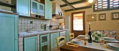 A kitchen with teal cabinets, a tiled backsplash, a stove, and a dining area with a table set for two.