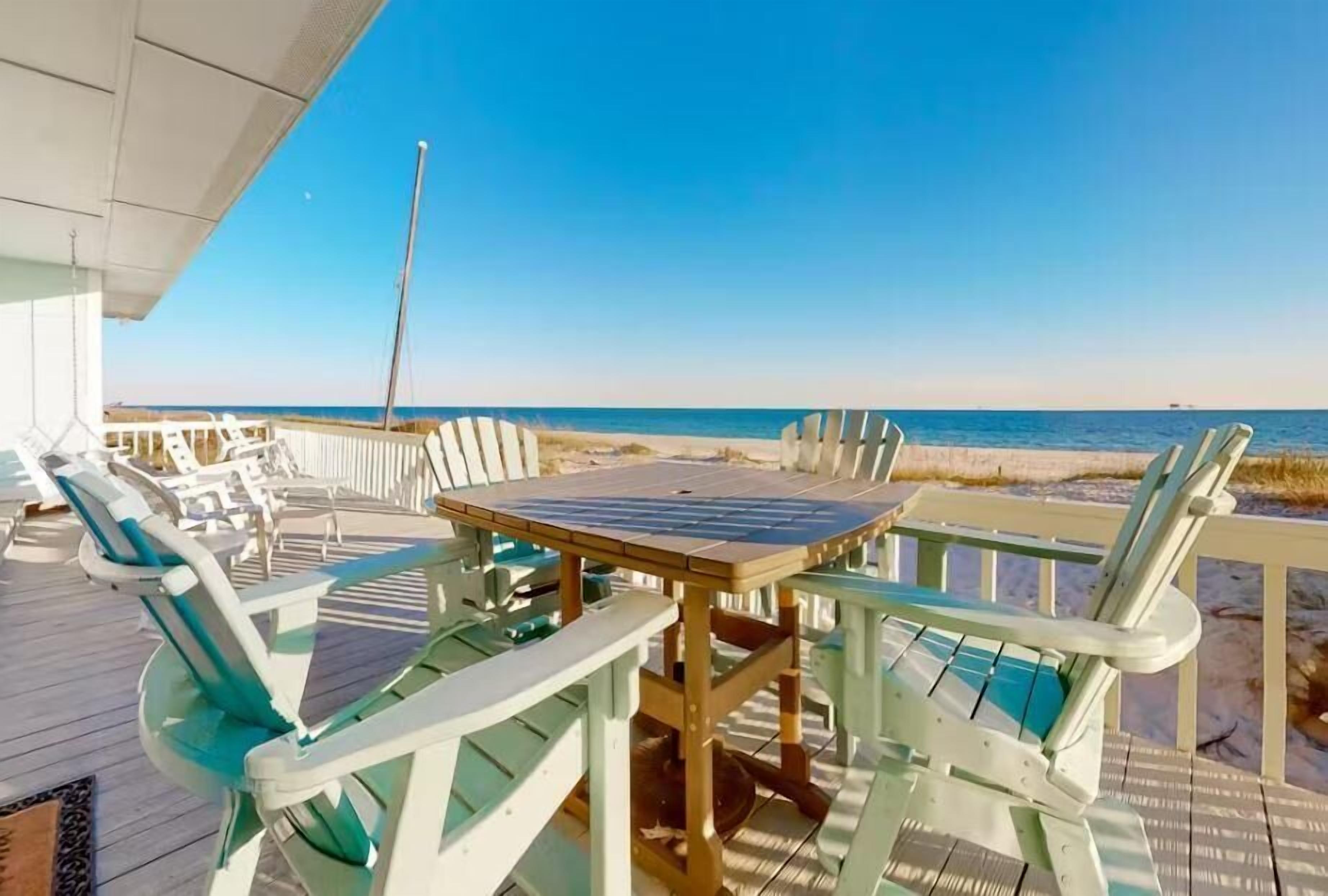 A deck with a table and chairs overlooking a beach.