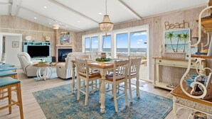A spacious living room with a large TV, comfortable seating, and a view of the ocean. - Barefoot Beach Beach House (Gulf Shores)