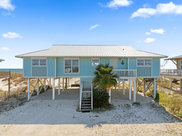 Ein zweistöckiges Strandhaus mit überdachter Veranda und einer kleinen Treppe zum Eingang.