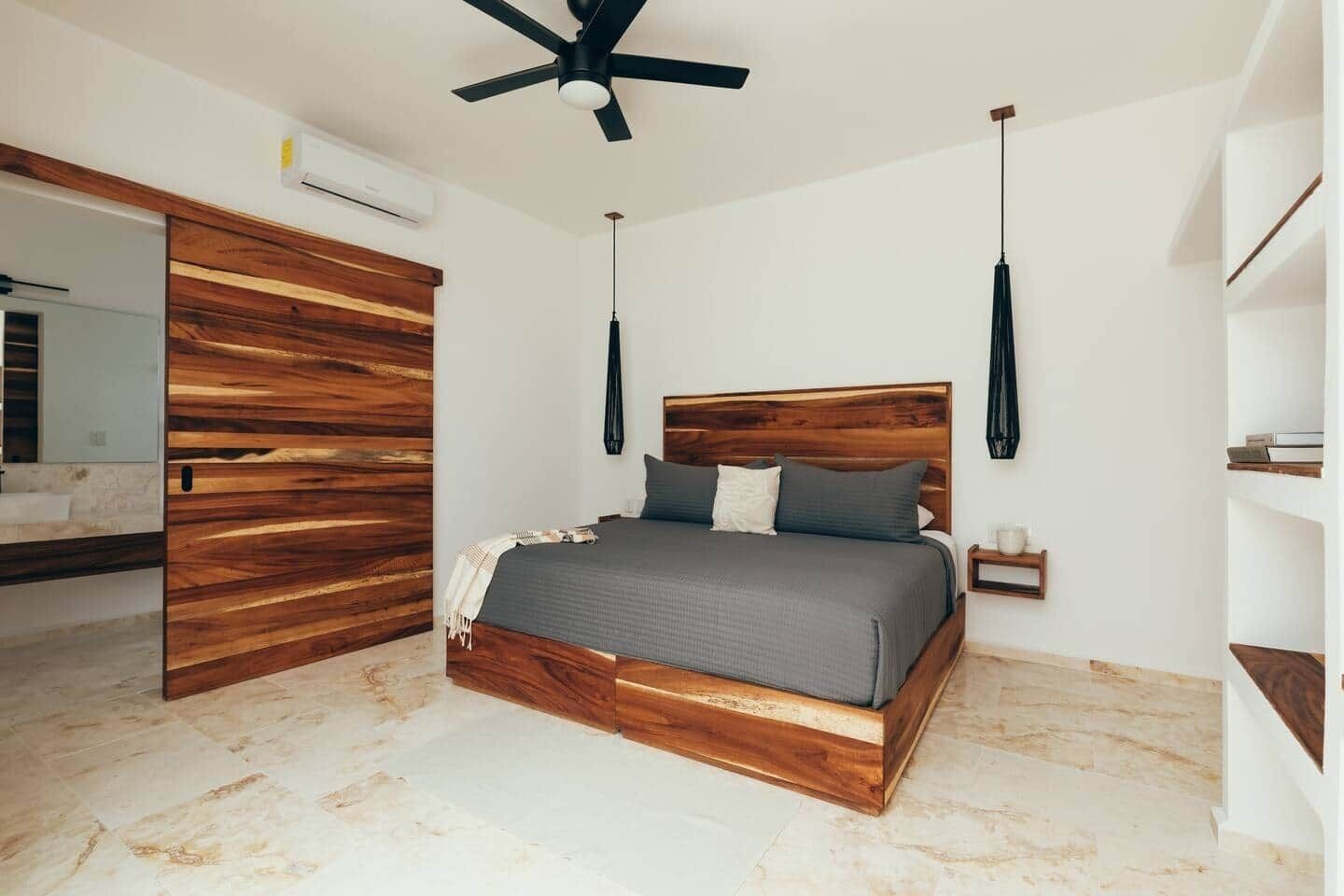 Une chambre à coucher avec une tête de lit en bois, un lit avec une literie grise, une table de chevet et une lampe suspendue.