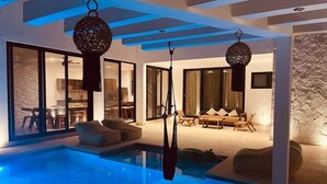 A modern indoor swimming pool with hanging lights, a seating area with cushions, and a stone wall. - New Villa Perfect For Groups. 20 Guests (Tulum Municipality)