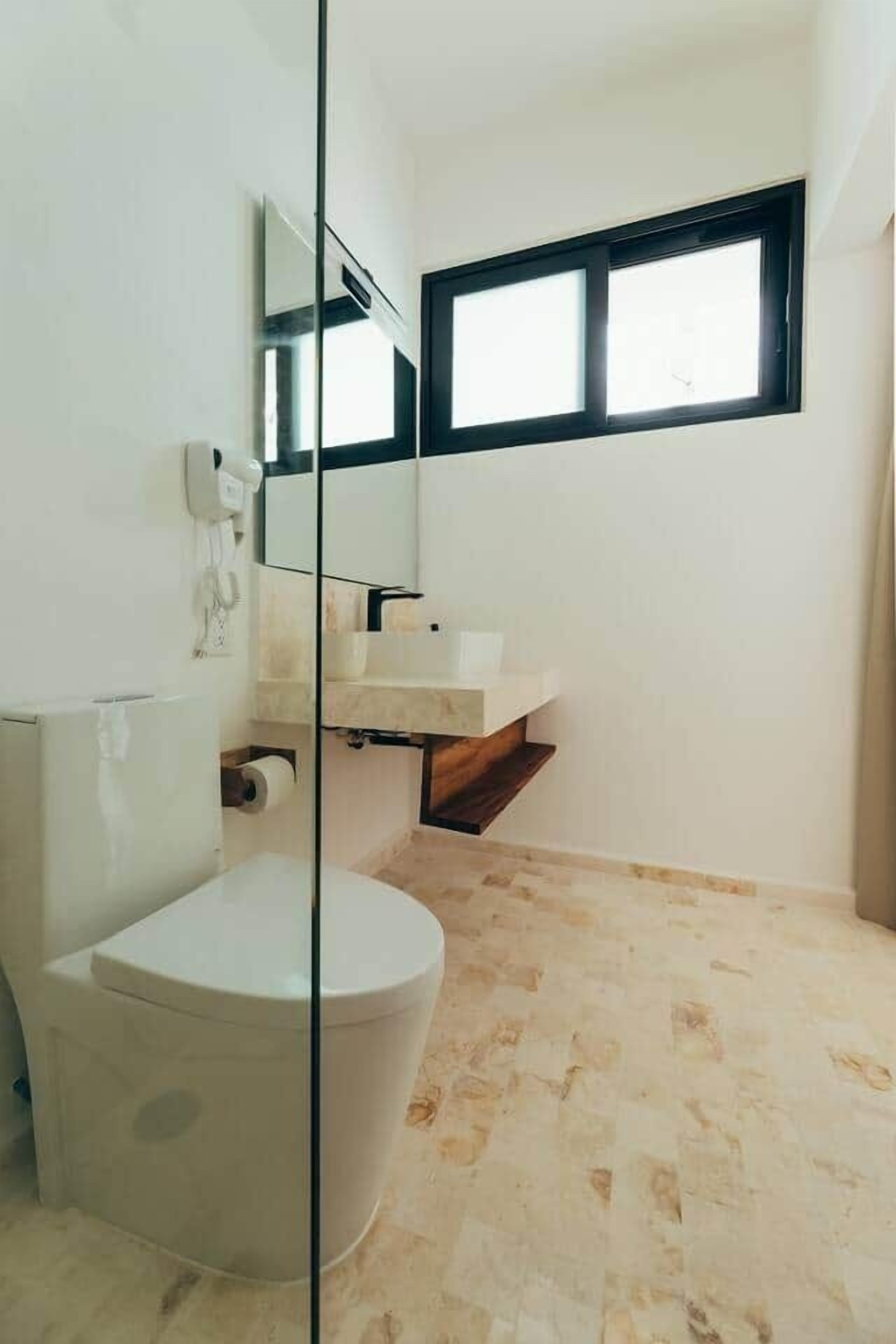A bathroom with a toilet, a sink, a mirror, and a window.