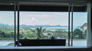 A modern room with a large window overlooking a scenic landscape including mountains, a body of water, and lush greenery. - Aroha Seaview Villa In Nature - Private Pool (Langkawi)