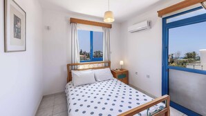 Een slaapkamer met een bed, een nachtkastje, een raam met gordijnen en een airconditioning.