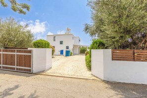 A white two-story house with a paved driveway leading to a blue door.