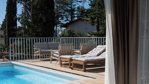 A poolside area with a wooden deck, lounge chairs, and a view of a house in the background. - VICE VERSA-SESASIDE BOUTIQUE APARTMENTS-APP NR.1 (Punat)