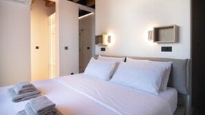 A neatly made bed with white linens and folded towels, a wooden ceiling, and a wall-mounted light fixture. - VICE VERSA-SESASIDE BOUTIQUE APARTMENTS-APP NR.1 (Punat)