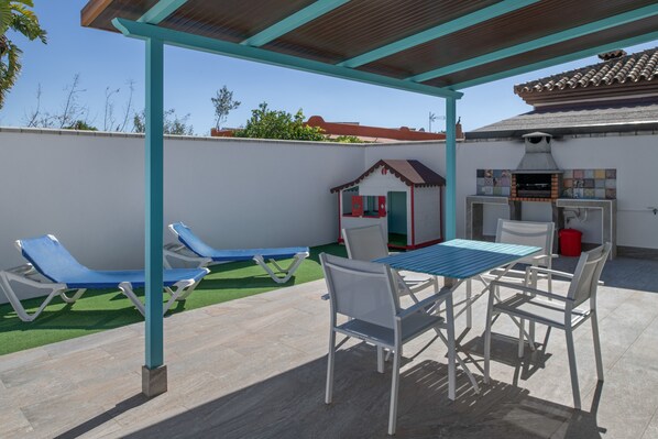 Une terrasse extérieure avec une table et des chaises, un barbecue et des fauteuils de jardin.