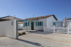 A white building with blue shutters, a white picket fence, and a gravel driveway.