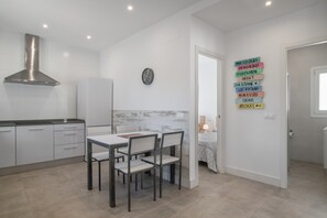Une cuisine moderne avec des armoires blanches, une hotte de cuisinière en acier inoxydable et un coin repas comprenant une table et des chaises.