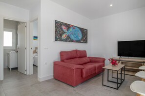 Un salon moderne avec un canapé rouge, un téléviseur à écran plat et un tableau accroché au mur.