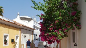 A narrow cobblestone street with buildings on either side, a tree with pink flowers, and a person sitting on the ground. - 'Beira Mar' Carvoeiro - Modern, intimate studio -Distant Ocean View - Fast Wifi (Carvoeiro)