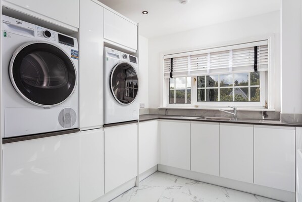 A modern kitchen with built-in appliances, a window with blinds, and a marble floor.