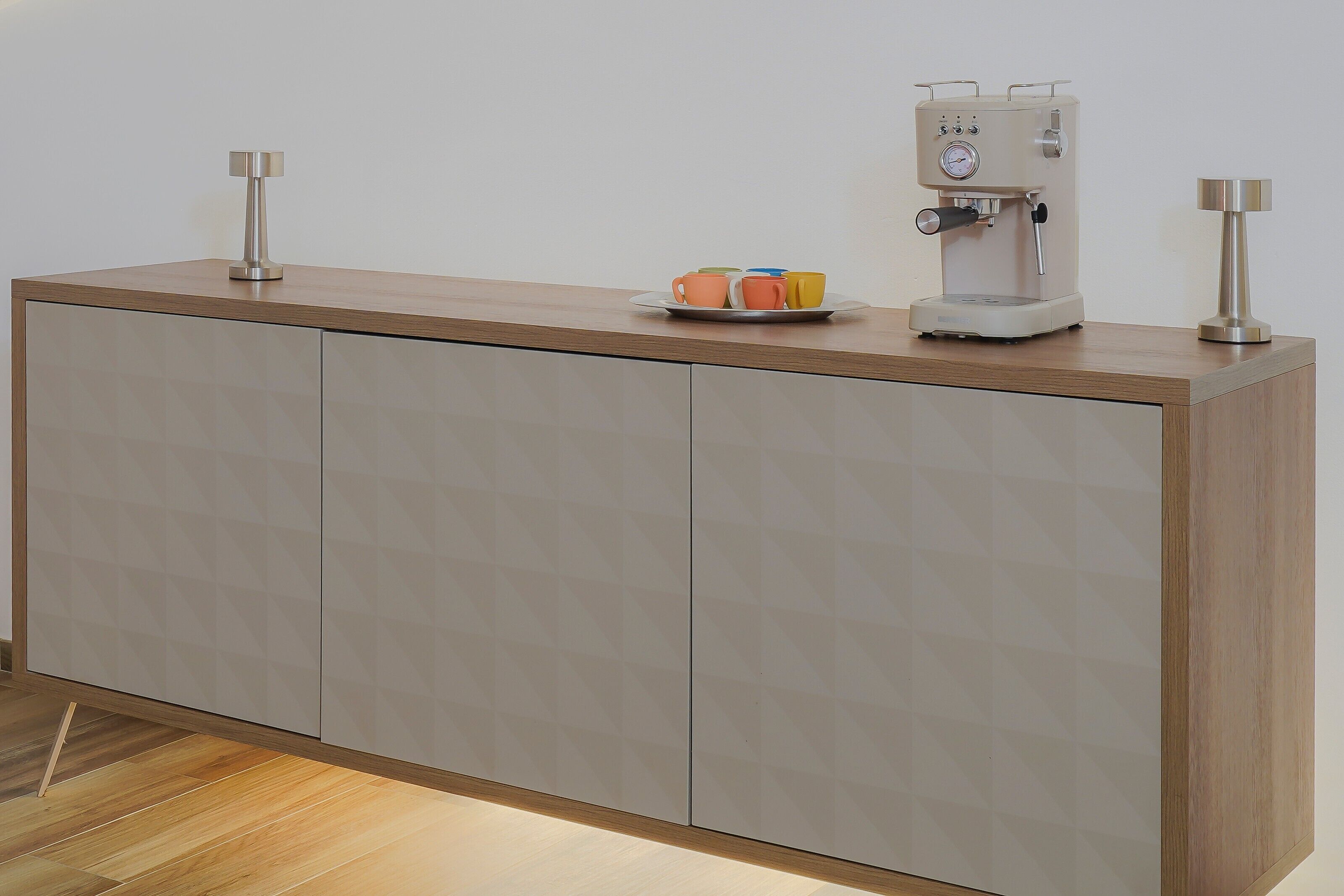 Een moderne keuken met een ingebouwde espresso machine, een klein bord met kleurrijke bekers, en een houten aanrecht.