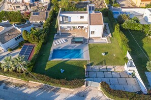 A modern two-story house with a swimming pool, solar panels, and a well-maintained lawn.