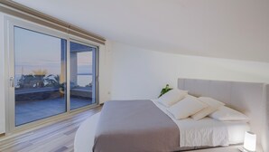 Ein Schlafzimmer mit einer großen Glasschiebetür, einem Bett mit weißer Bettwäsche und einem Nachttisch mit Lampe.