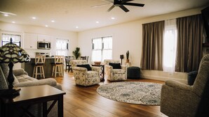 A spacious living room with a round rug, two armchairs, a coffee table, and a dining area with a kitchen in the background.