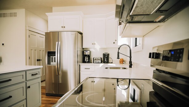 A modern kitchen with stainless steel appliances, white cabinetry, and a glass dining table.